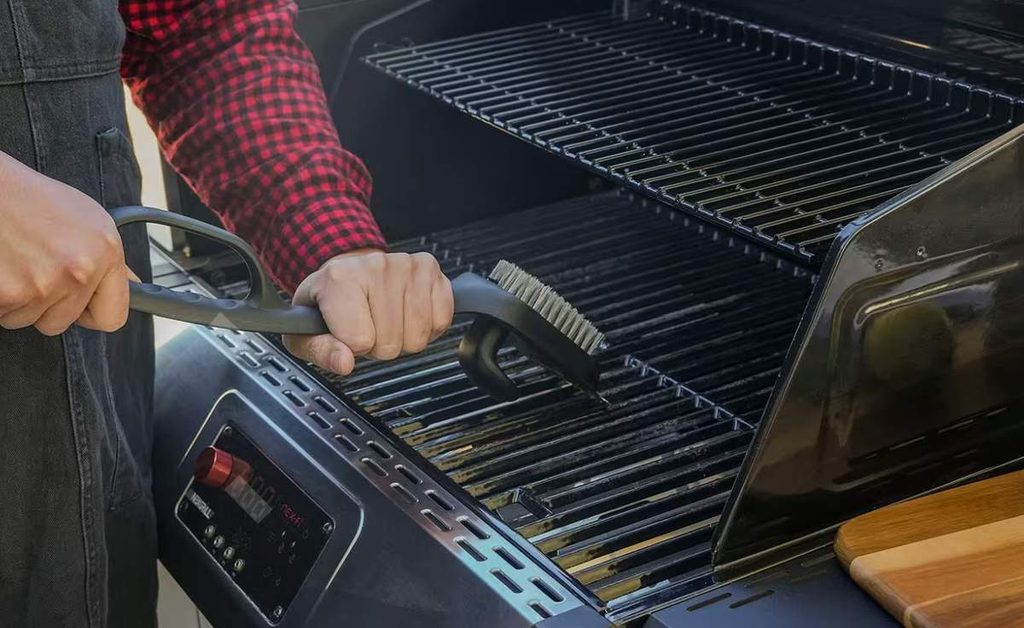 Person cleaning propane BBQ grill grates with a grill brush